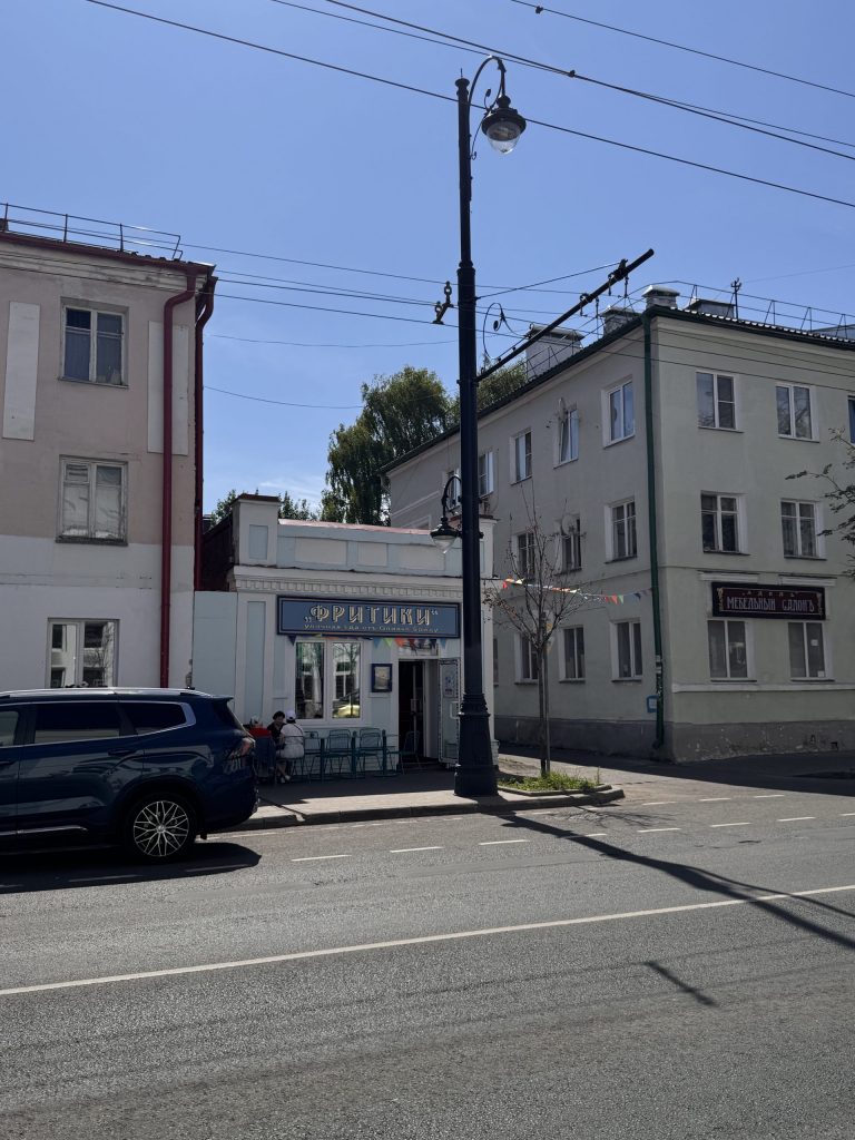 Вывеска "под старину" на кафе "Фритики" со столиками прямо на улице в европейском стиле